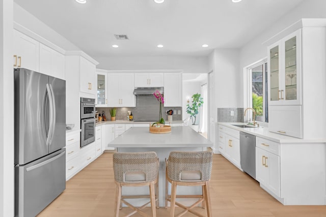 kitchen with a breakfast bar, white cabinetry, sink, stainless steel appliances, and light wood-type flooring