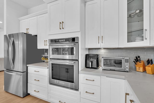 kitchen featuring white cabinetry, stainless steel appliances, light hardwood / wood-style floors, and backsplash