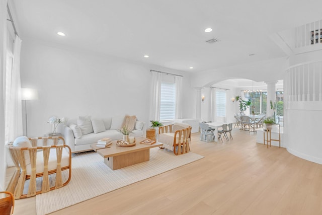 living room featuring decorative columns, ornamental molding, a wealth of natural light, and light hardwood / wood-style floors