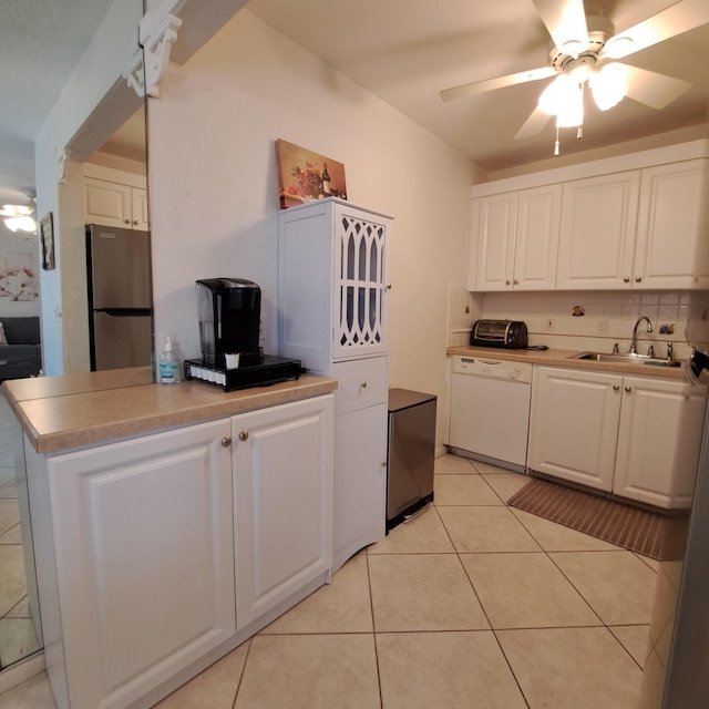 kitchen featuring dishwasher, sink, light tile patterned floors, white cabinets, and stainless steel fridge