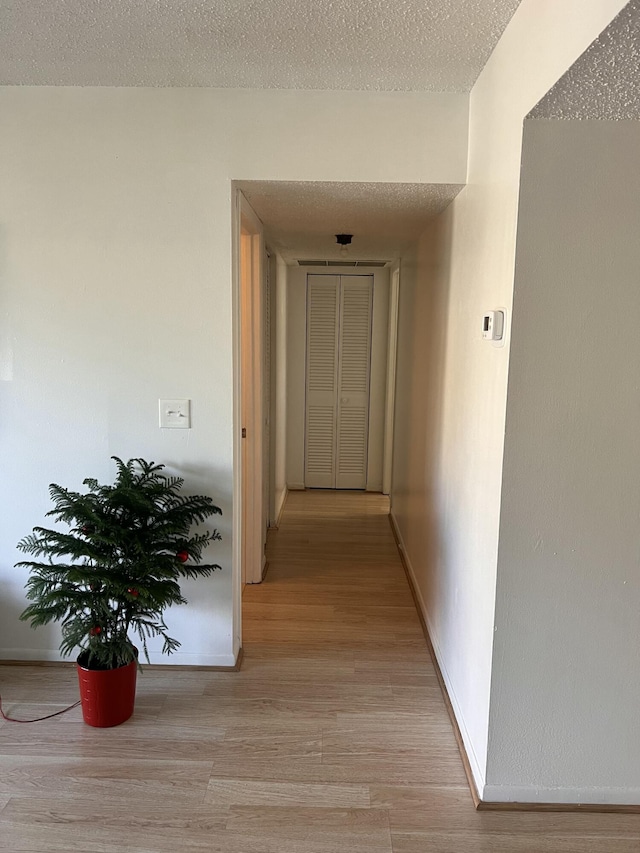 hallway with light hardwood / wood-style floors and a textured ceiling