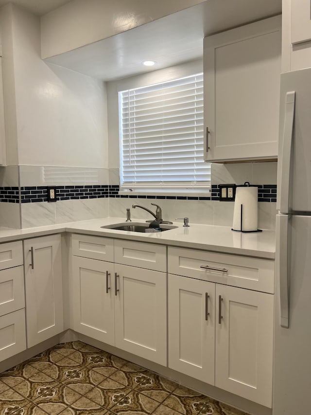 kitchen featuring tile patterned flooring, white cabinetry, sink, backsplash, and stainless steel fridge