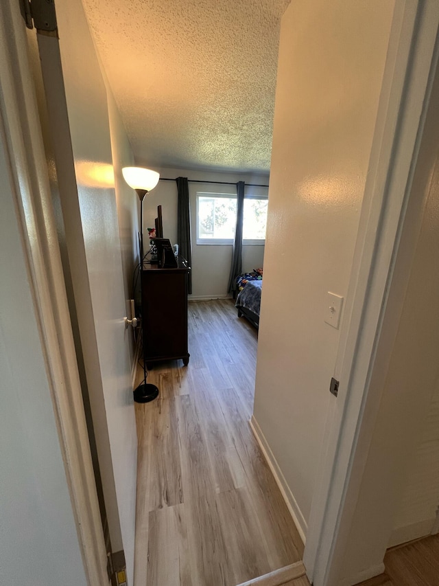 hallway with a textured ceiling and light hardwood / wood-style floors