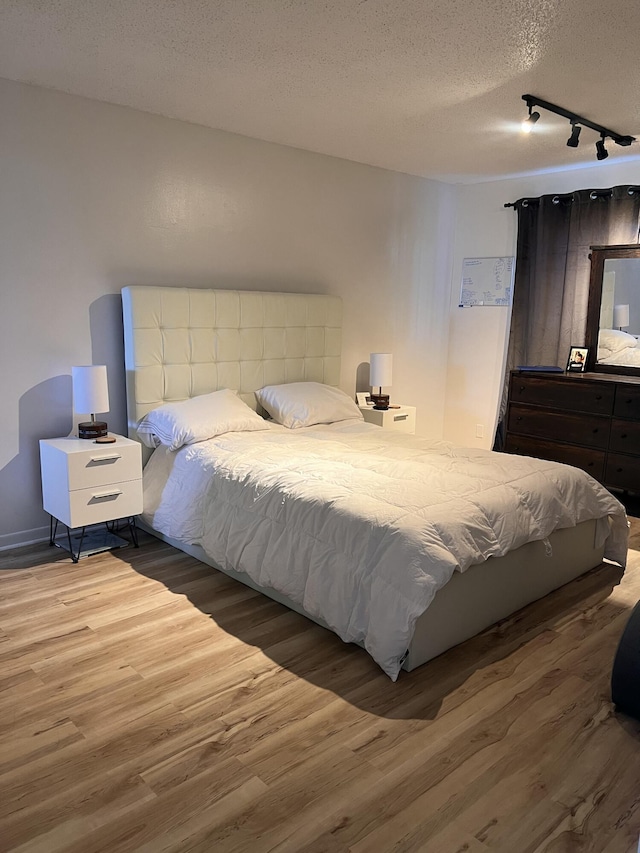 bedroom featuring rail lighting, a textured ceiling, and hardwood / wood-style floors