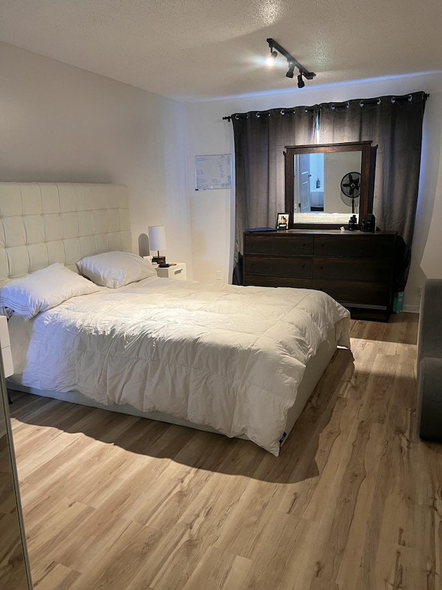 bedroom with a textured ceiling, rail lighting, and light hardwood / wood-style floors