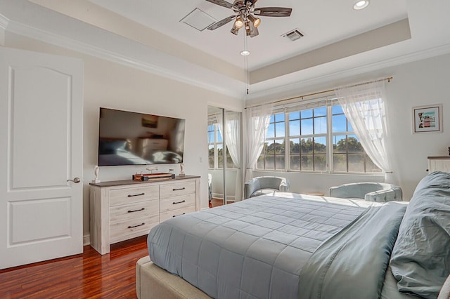 bedroom featuring a tray ceiling, dark wood-type flooring, ornamental molding, and ceiling fan