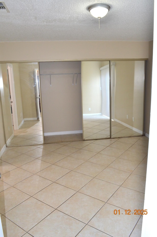 unfurnished bedroom with a textured ceiling, light tile patterned floors, and a closet