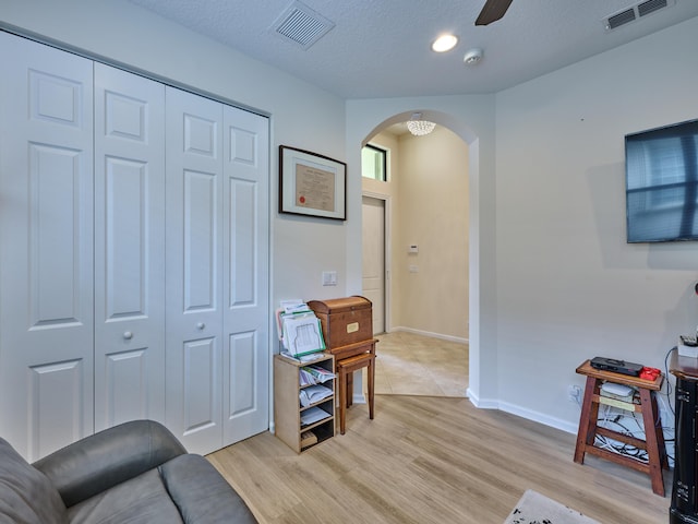 living area featuring light wood-type flooring, ceiling fan, and a textured ceiling