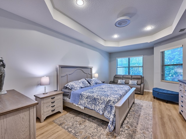 bedroom featuring a raised ceiling, a textured ceiling, and light hardwood / wood-style floors