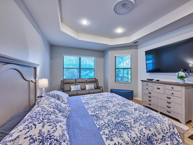 bedroom featuring a textured ceiling, wood-type flooring, and a tray ceiling