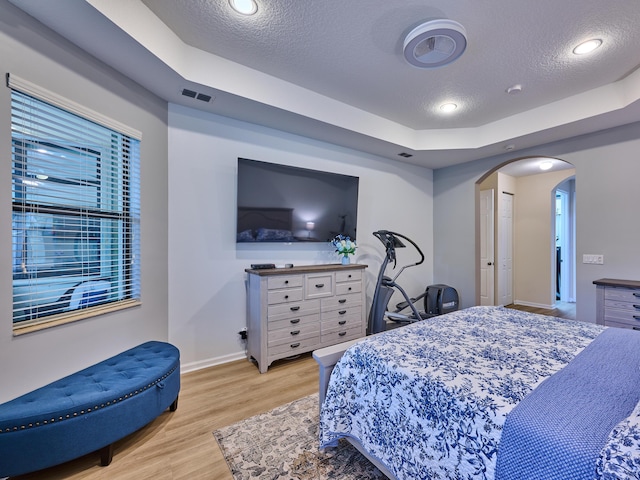 bedroom with a textured ceiling, light hardwood / wood-style flooring, and a raised ceiling