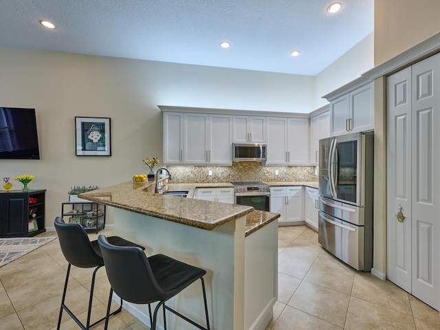 kitchen with stainless steel appliances, dark stone countertops, a kitchen breakfast bar, sink, and kitchen peninsula