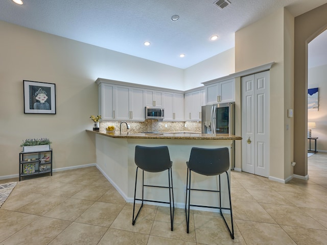 kitchen with white cabinetry, stainless steel appliances, dark stone countertops, kitchen peninsula, and a breakfast bar area