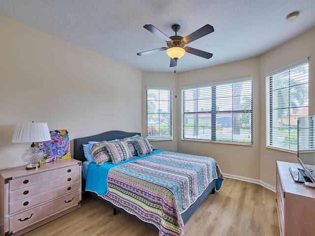 bedroom with a textured ceiling, ceiling fan, light hardwood / wood-style flooring, and multiple windows