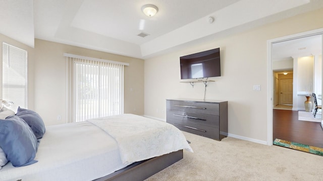 bedroom with a raised ceiling and light colored carpet