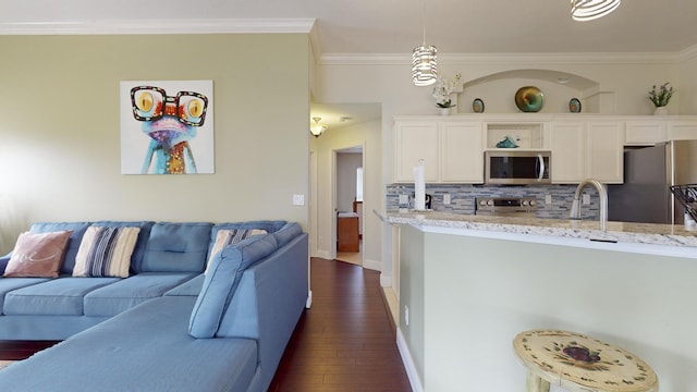 kitchen with pendant lighting, stainless steel appliances, backsplash, light stone counters, and crown molding