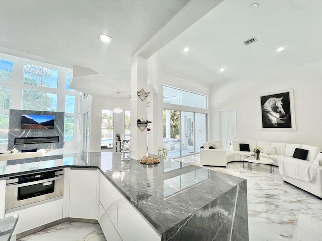 kitchen with a notable chandelier, dark stone countertops, a towering ceiling, stainless steel oven, and white cabinets