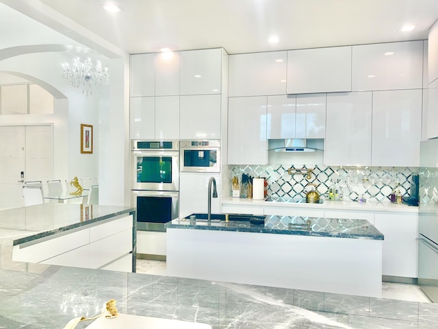 kitchen featuring decorative backsplash, stainless steel double oven, white cabinets, and dark stone countertops