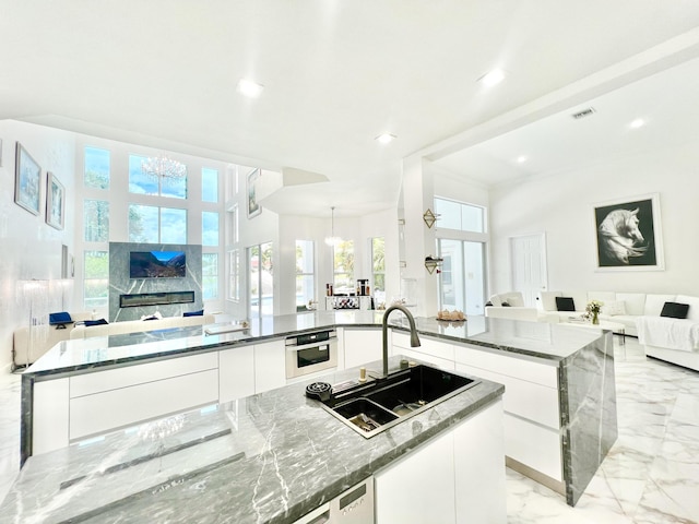 kitchen with white cabinetry, dark stone counters, oven, a chandelier, and sink