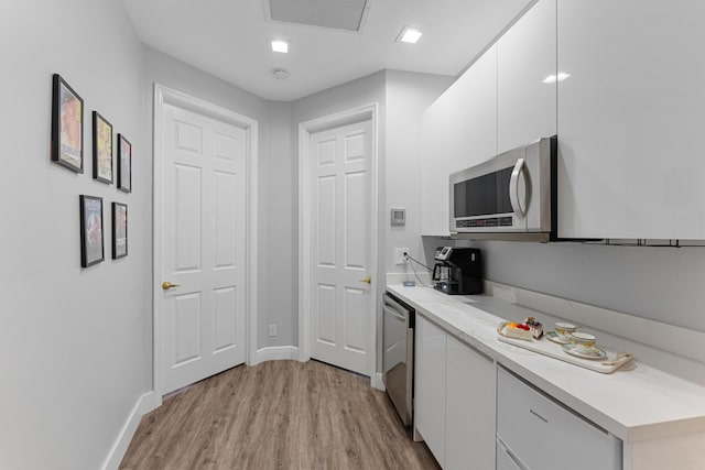 kitchen with light stone countertops, white cabinets, appliances with stainless steel finishes, and light hardwood / wood-style flooring