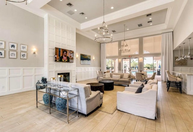 living room featuring light wood-type flooring, crown molding, a high ceiling, and a notable chandelier