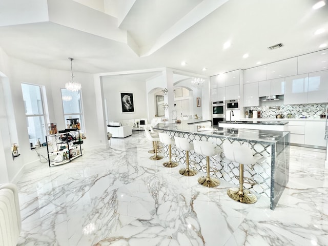 kitchen featuring pendant lighting, white cabinets, stainless steel double oven, decorative backsplash, and a kitchen breakfast bar