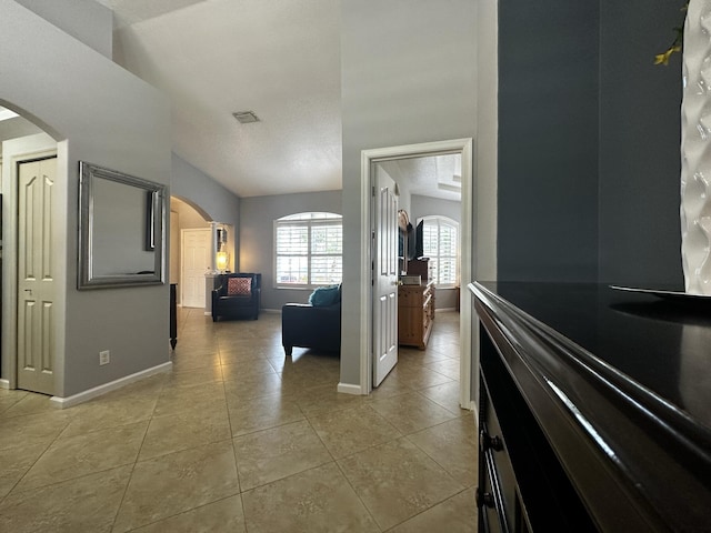 hall with lofted ceiling, light tile patterned flooring, and a textured ceiling