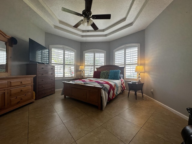 tiled bedroom featuring a textured ceiling, ceiling fan, and a raised ceiling