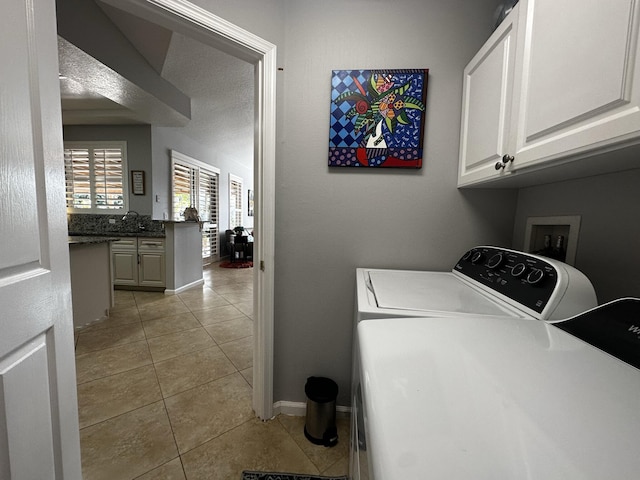 clothes washing area featuring washing machine and dryer, cabinets, light tile patterned flooring, and sink