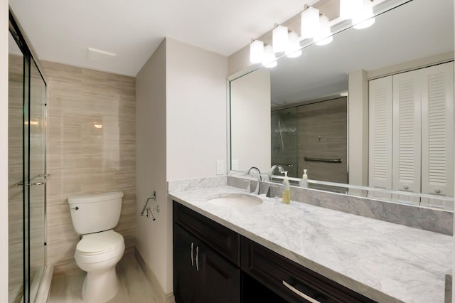 bathroom featuring toilet, vanity, tile walls, and a shower with door