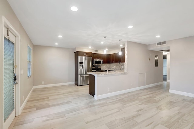 kitchen with tasteful backsplash, decorative light fixtures, light stone countertops, appliances with stainless steel finishes, and dark brown cabinets