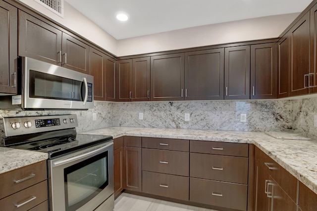 kitchen with stainless steel appliances, dark brown cabinets, tasteful backsplash, and light stone counters