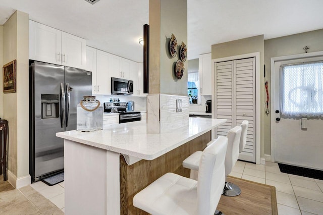 kitchen featuring a kitchen bar, appliances with stainless steel finishes, light tile patterned flooring, light stone countertops, and white cabinets