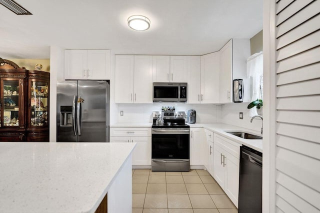 kitchen featuring light tile patterned floors, appliances with stainless steel finishes, tasteful backsplash, white cabinets, and sink