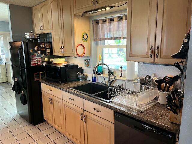 kitchen with a sink, black appliances, dark stone countertops, and light tile patterned floors