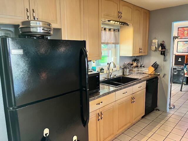 kitchen with black appliances, light tile patterned flooring, dark countertops, and a sink