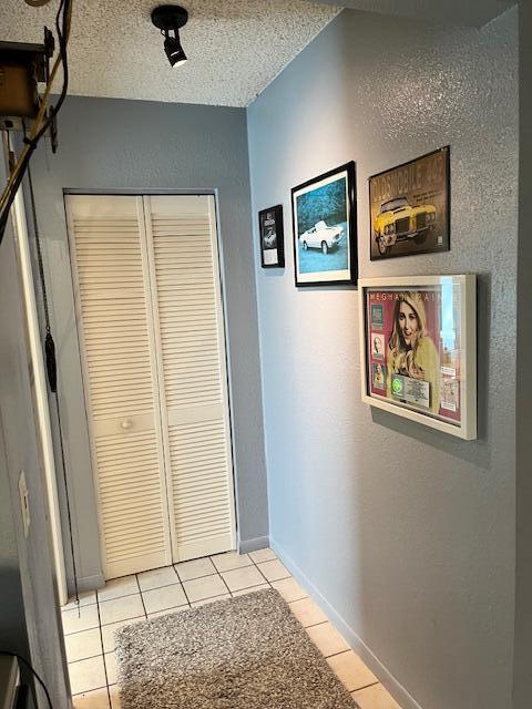 corridor featuring light tile patterned floors, baseboards, a textured ceiling, and a textured wall