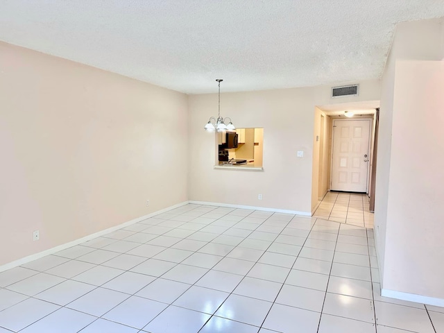 tiled empty room with an inviting chandelier and a textured ceiling