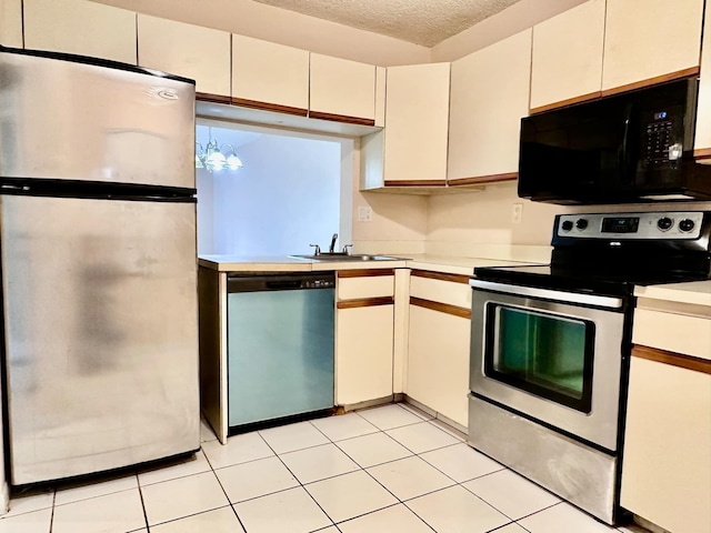 kitchen with sink, light tile patterned floors, stainless steel appliances, a textured ceiling, and white cabinets