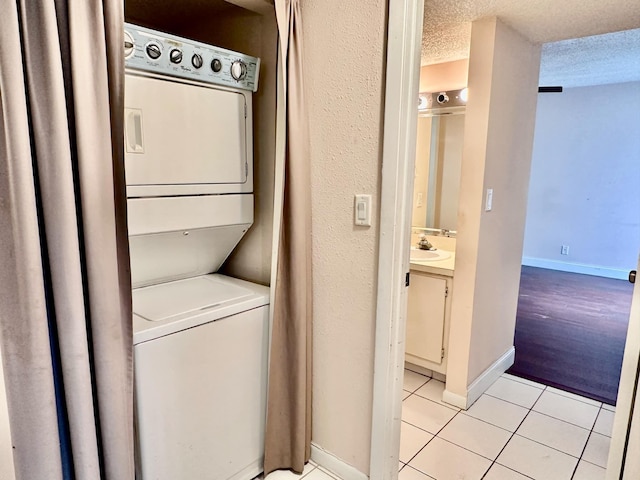 clothes washing area with sink, a textured ceiling, light tile patterned floors, and stacked washer and clothes dryer