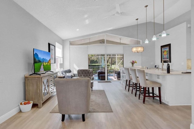 living room featuring lofted ceiling, light wood-type flooring, ceiling fan with notable chandelier, and a textured ceiling