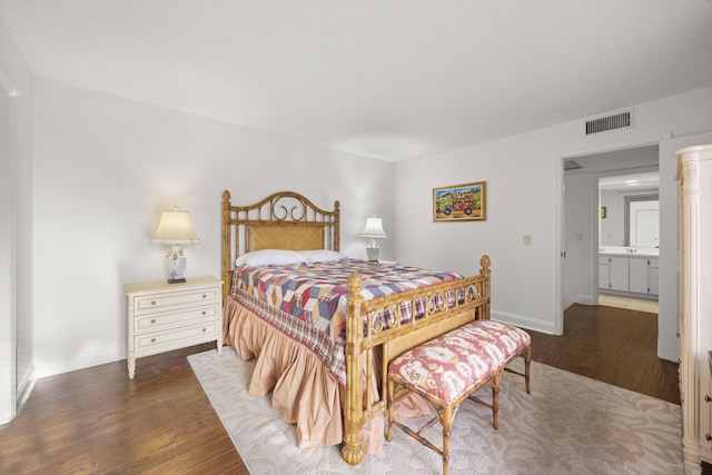 bedroom featuring dark wood-type flooring and ensuite bath