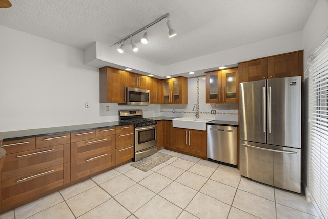 kitchen featuring tasteful backsplash, sink, light tile patterned floors, stainless steel appliances, and a textured ceiling