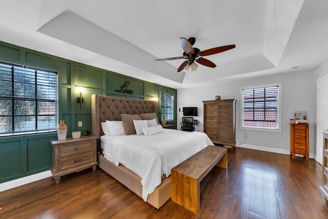 bedroom with ceiling fan, dark hardwood / wood-style flooring, multiple windows, and a tray ceiling