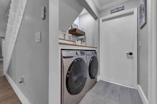 clothes washing area with light wood-type flooring, washer and dryer, and ornamental molding