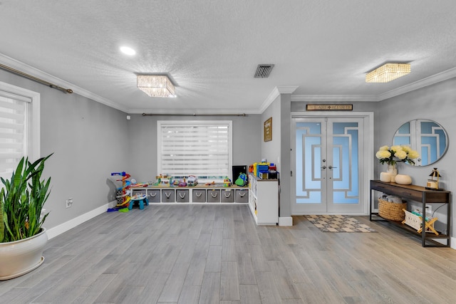 rec room featuring ornamental molding, a textured ceiling, light hardwood / wood-style flooring, and french doors