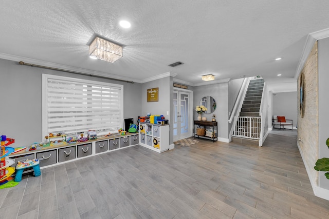 game room featuring crown molding, light wood-type flooring, a textured ceiling, and french doors