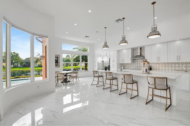 kitchen with pendant lighting, white cabinetry, stainless steel built in fridge, and wall chimney range hood