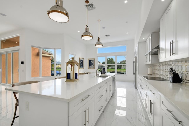 kitchen featuring white cabinetry, backsplash, decorative light fixtures, and a large island with sink