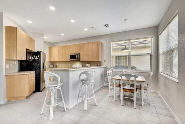 kitchen with appliances with stainless steel finishes, decorative light fixtures, a kitchen bar, kitchen peninsula, and light brown cabinets